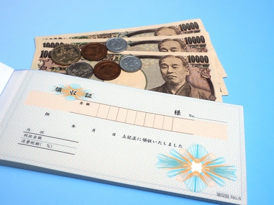 水色の背景に領収書とお金が置かれている写真
