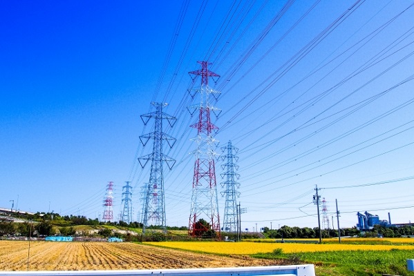 青空をバックにした田んぼに立つ送電塔の写真